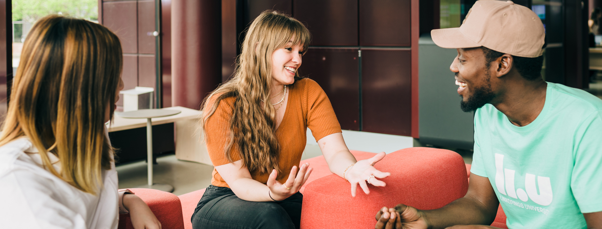 Tre studenter som sitter i en öppen miljö i färgglada soffor.