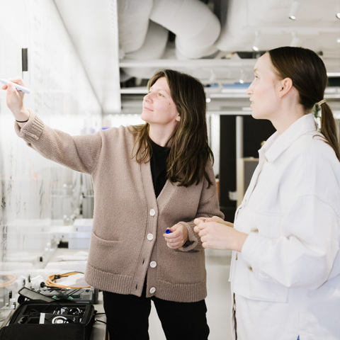 Två kvinnor som arbetar tillsammans vid en whiteboardtavla