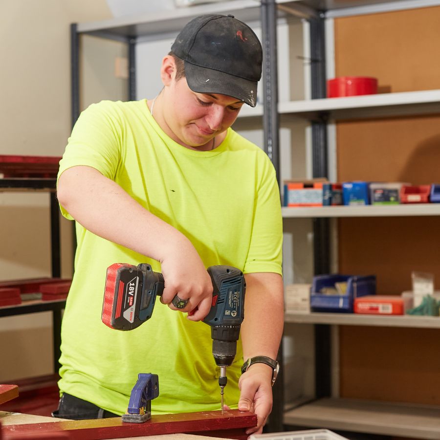 Pojke med gul tröja som står och skruvar.