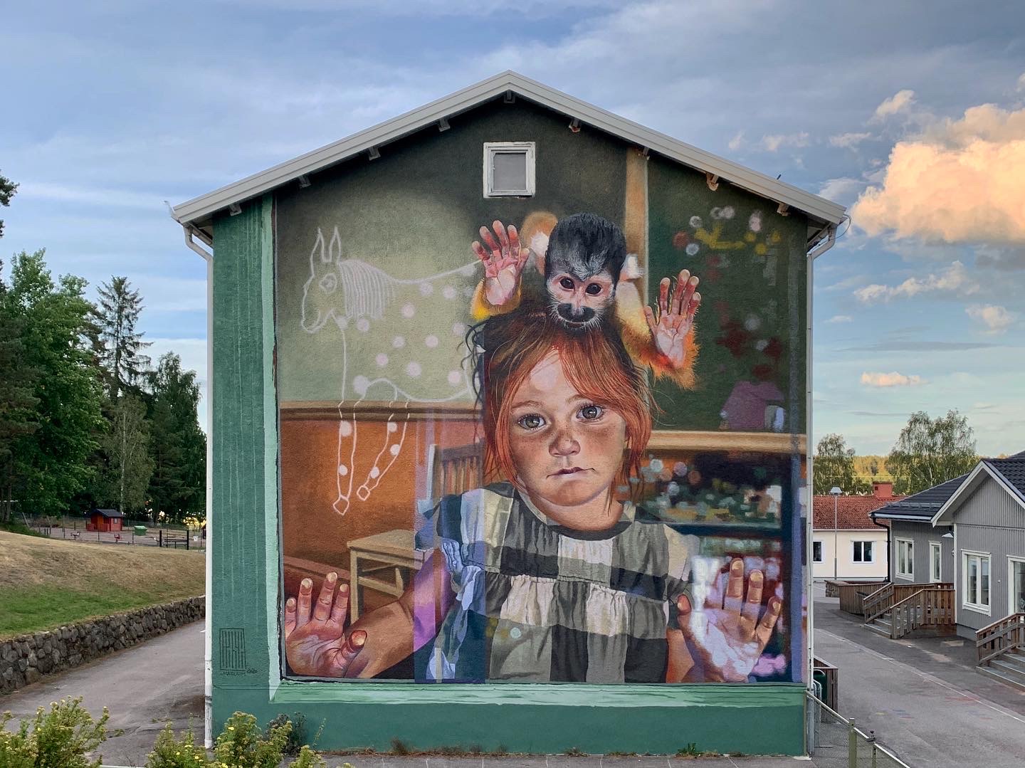 Väggmålning föreställande en flicka med rött hår som håller händerna mot fönsterrutan som hon tittar ut igenom. En apa sitter på hennes huvud.  