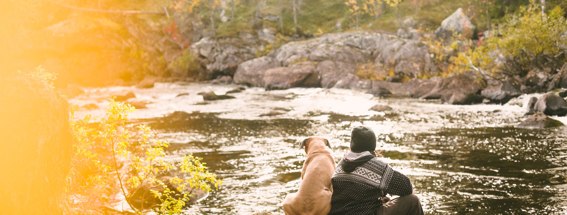 Person med hund som sitter vid vattnet. 