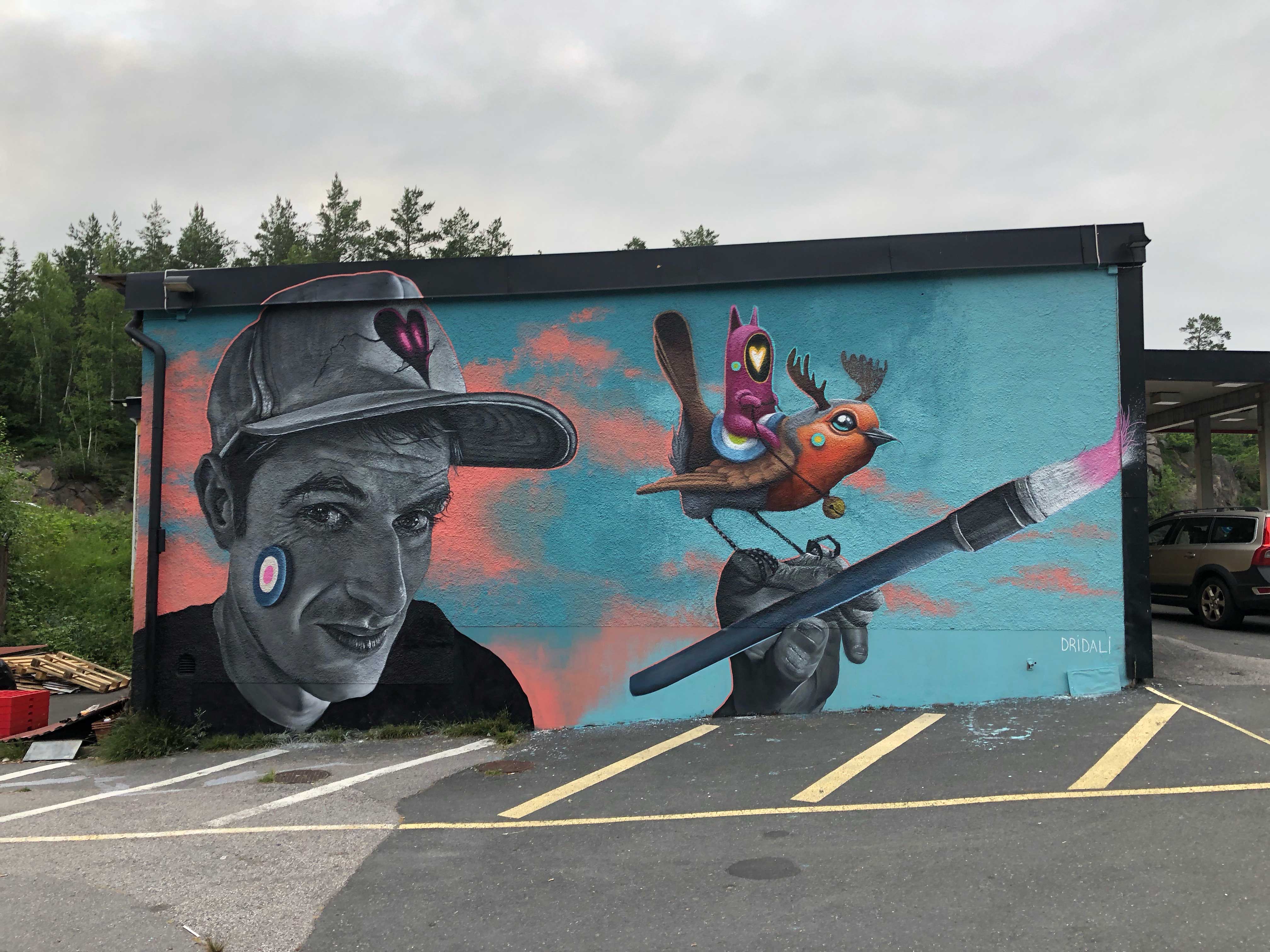 Väggmålning föreställande man i keps som håller i en pensel med rosa färg.