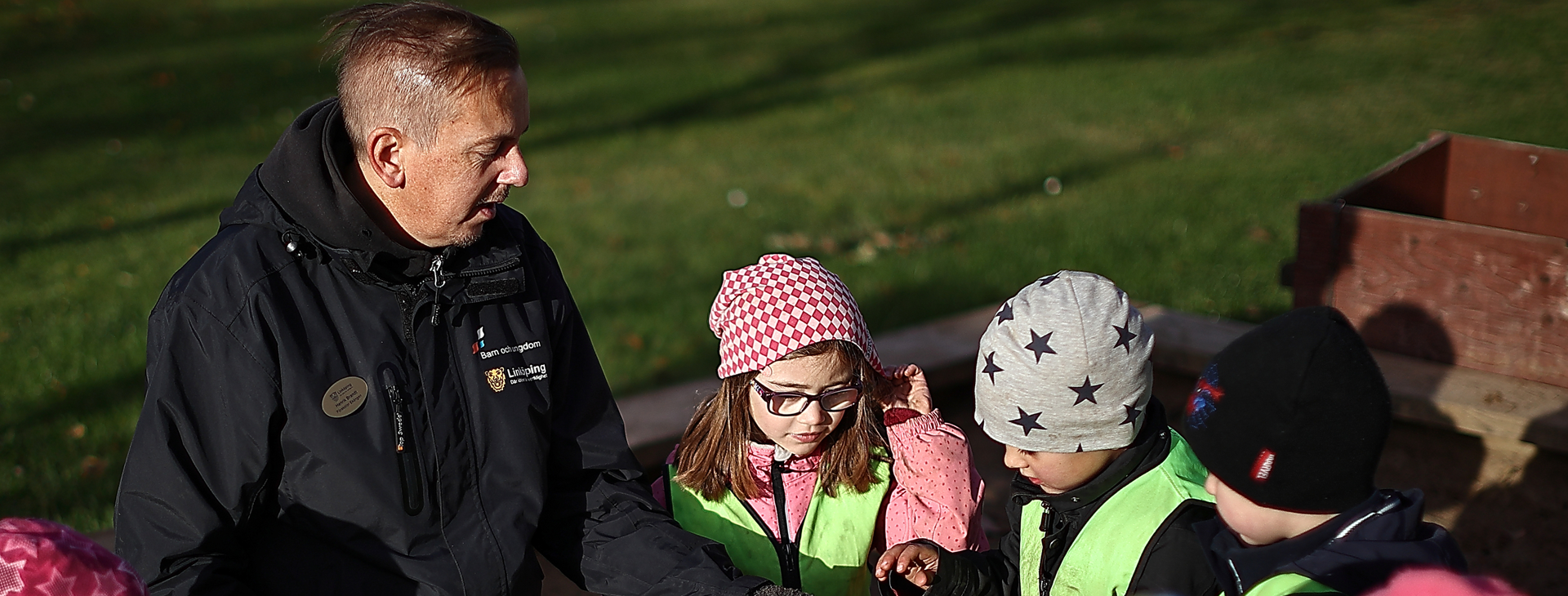 En manlig förskollärare interagerar med barnen i en utomhusmiljö.
