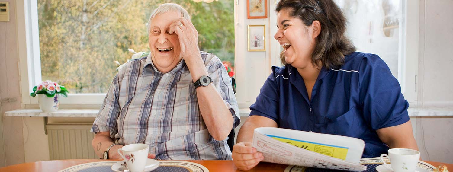Man och hemtjänstpersonal som sitter och fikar och skrattar. 