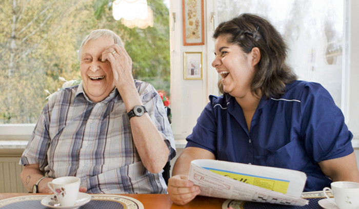 Äldre man och kvinna från hemtjänst skrattar tillsammans.
