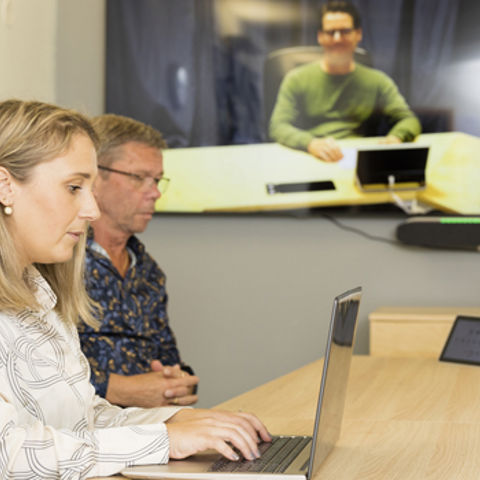 Tre personer i möte, varav en är med via skärm och de andra tittar in i en dator.