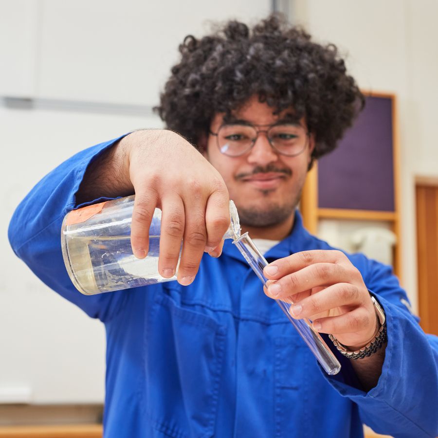 Pojke med lockigt hår och skägg med provrör i handen. 