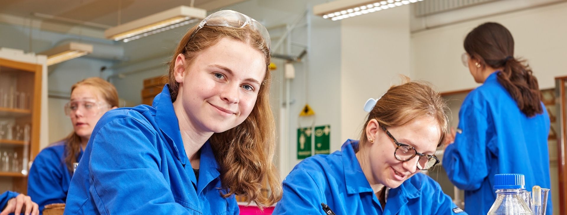 Killer som sitter i en labbsal i naturkunskapen och har blå rock på sig.