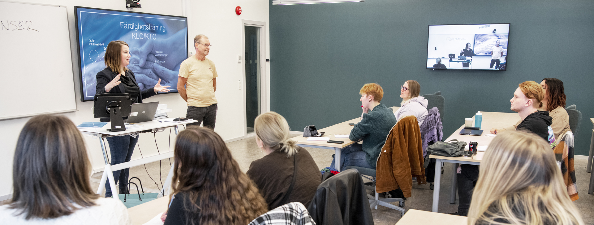 Två lärare undervisar studenter i ett klassrum.