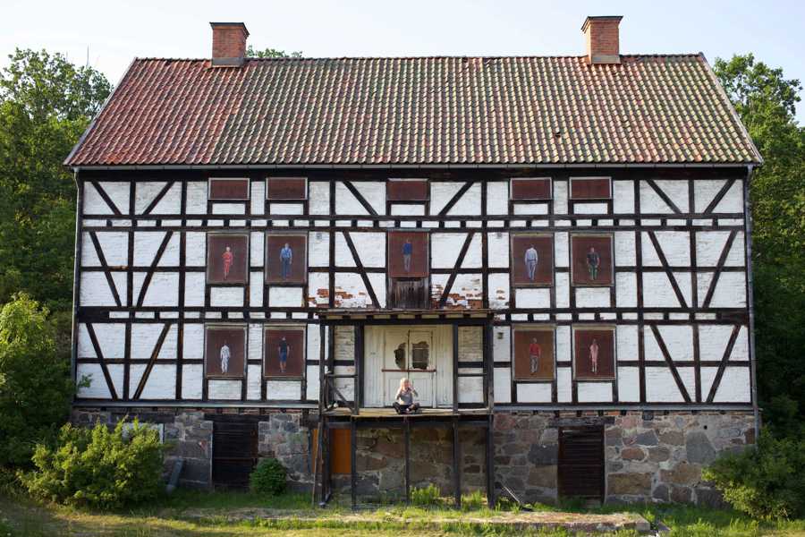 Vitt korsvirkeshus med porträtt målade på igensatta fönster.