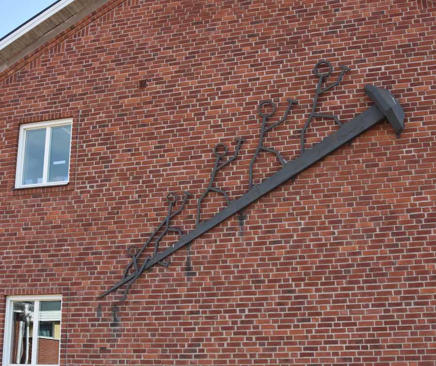 Stor smid spik med gubbar som klättrar uppåt. Placerad på röd tegelvägg.