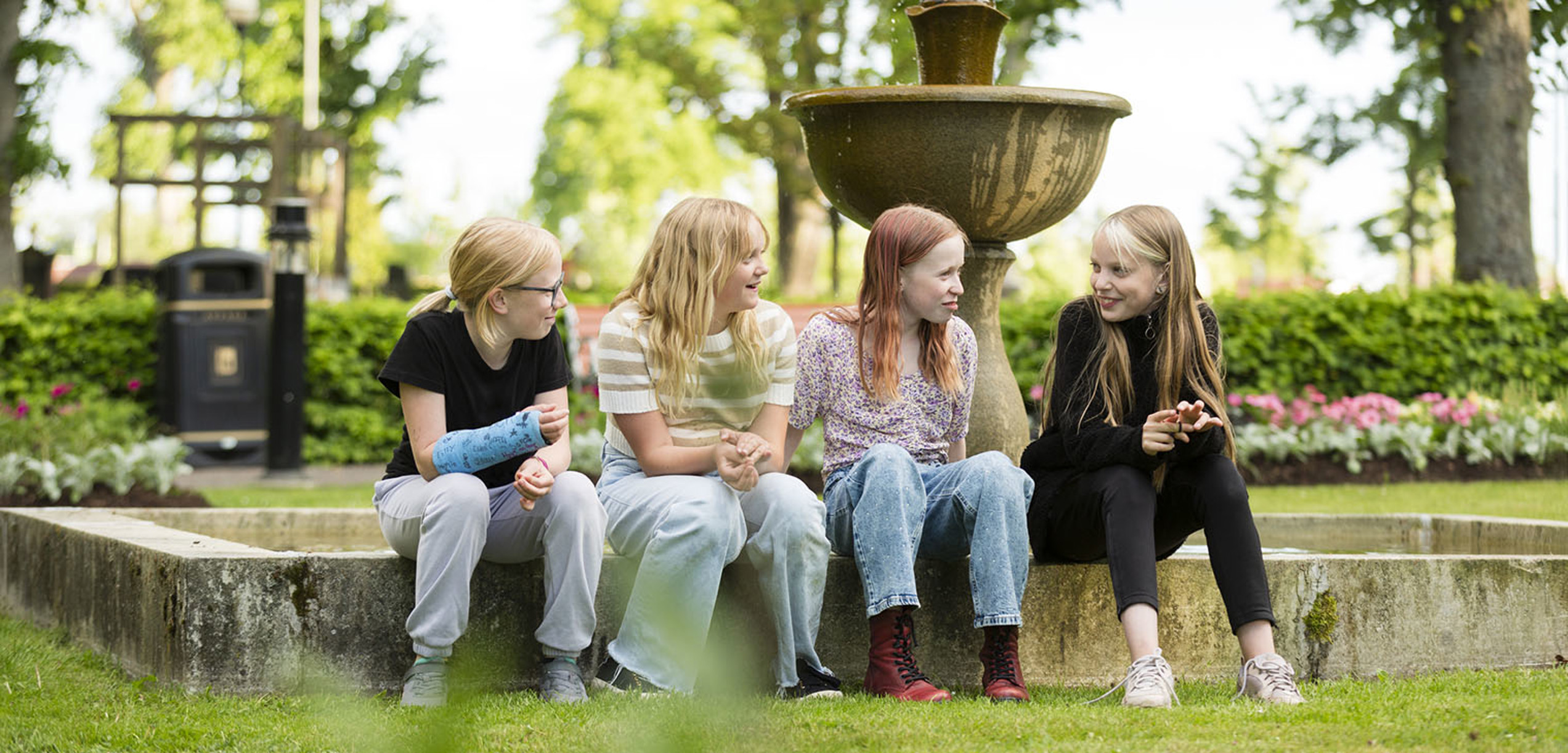 Fyra ungdomar som sitter framför en fontän. 