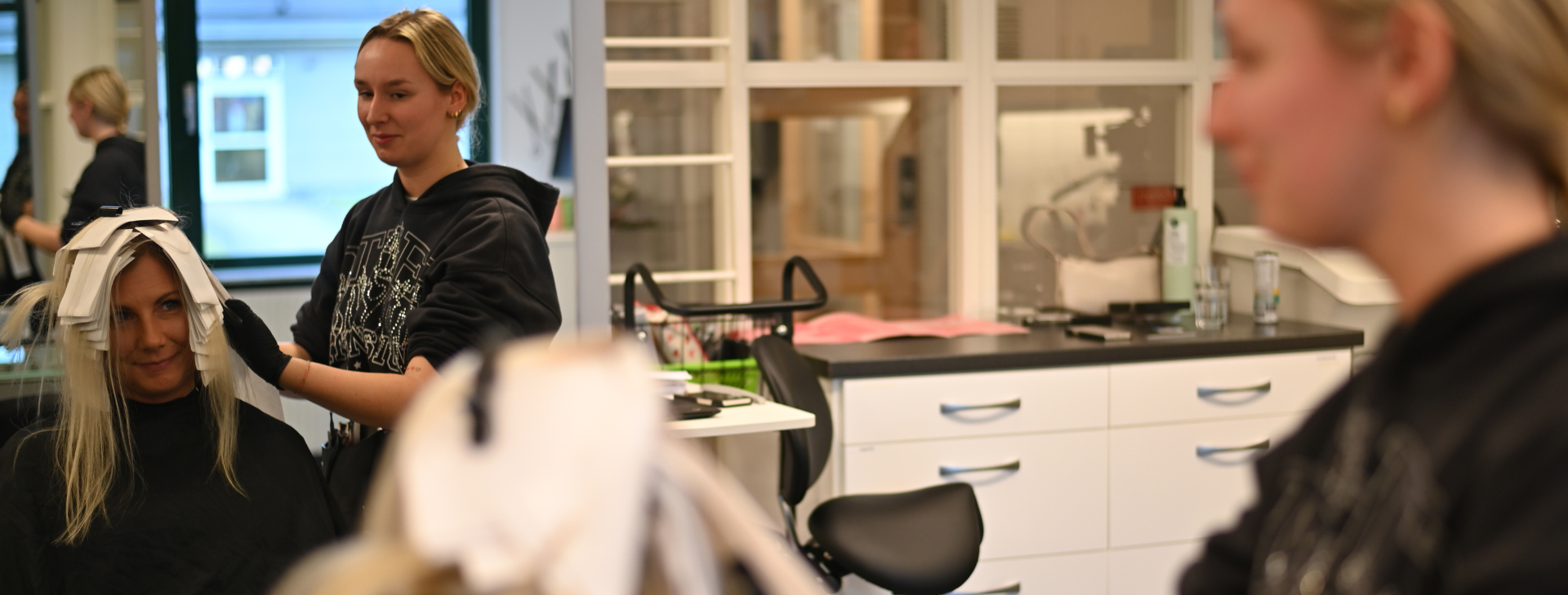 Dockhuvud med rosa hår och elever som sitter runt ett bord och arbetar.