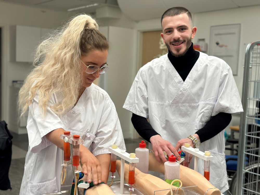 Två vårdelever som tränar på att ta blodprov på en docka