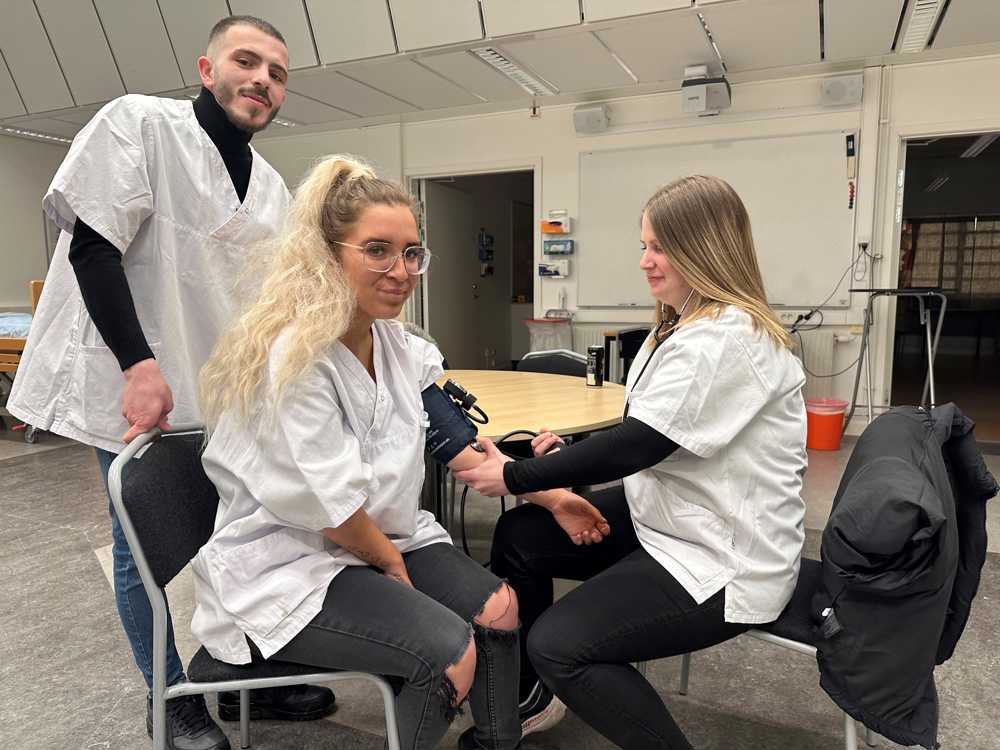Tre vårdelever, två kvinnor och en man, som tar blodtrycket
