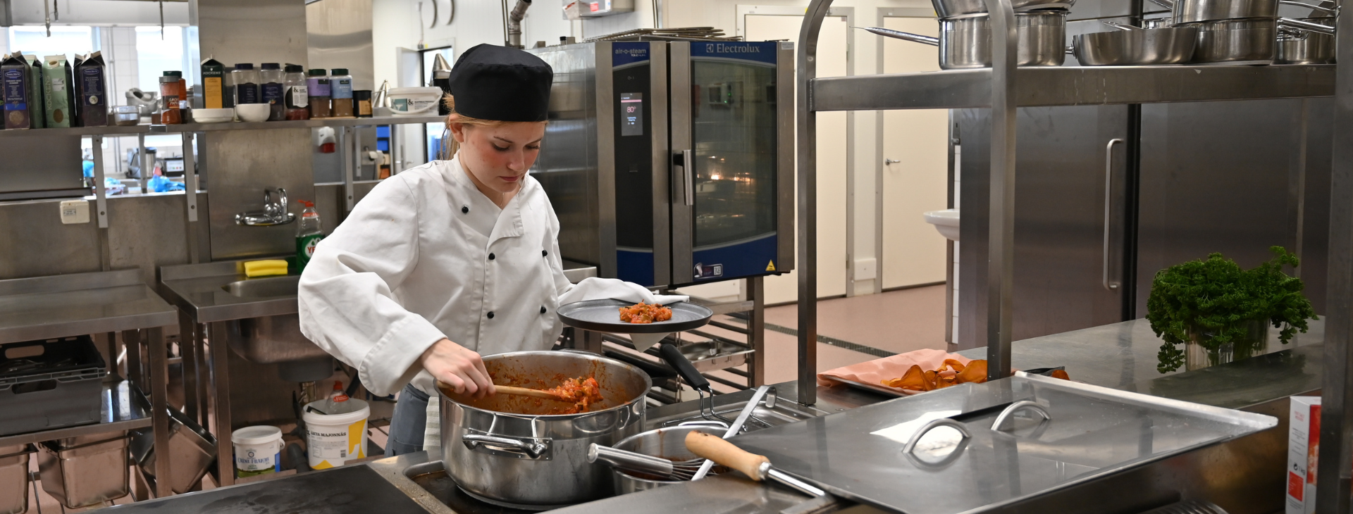 Tjej med kockmössa i ett kök. 