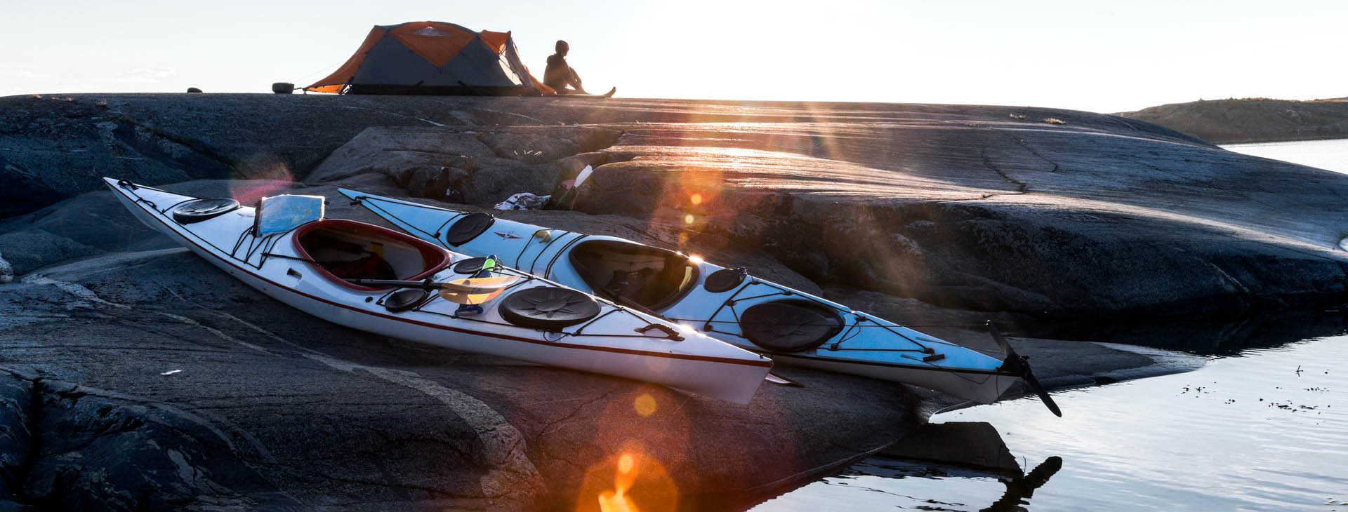 Kajaker på klippa med tältare i bakgrunden. 