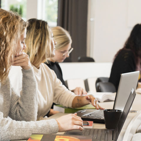 Fem studenter som sitter i en föreläsningssal med sina laptops.