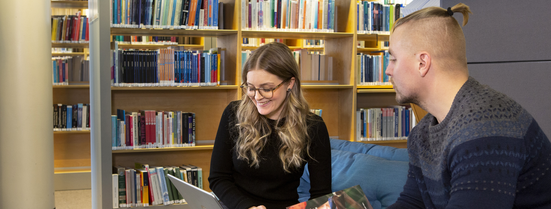 Bild på två studenter som sitter i en lugn biblioteksmiljö och tittar på en laptopskärm