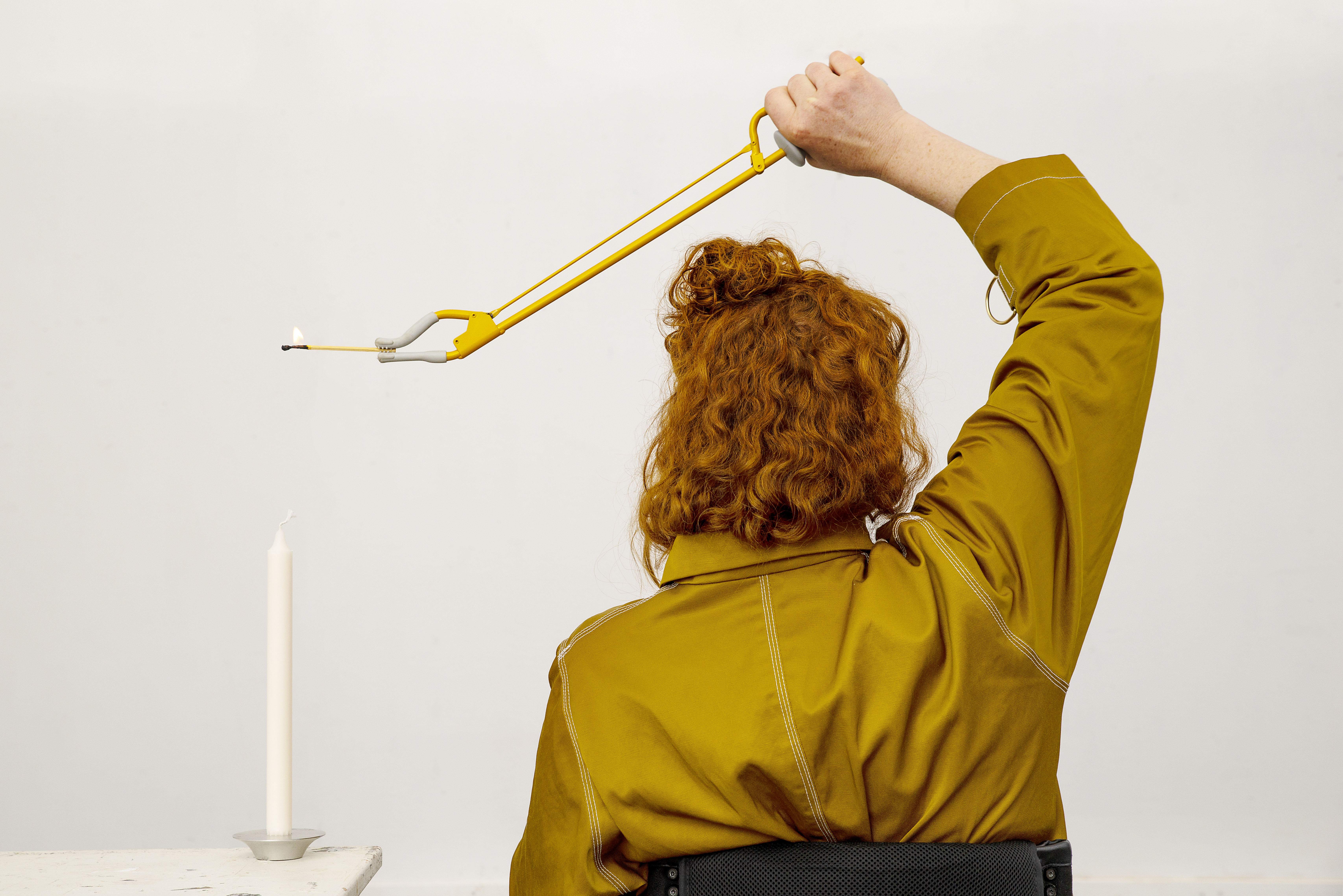 Bildtolkning: En kvinna i rullstol håller en griptång över huvudet. I griptången håller hon en brinnande tändsticka.