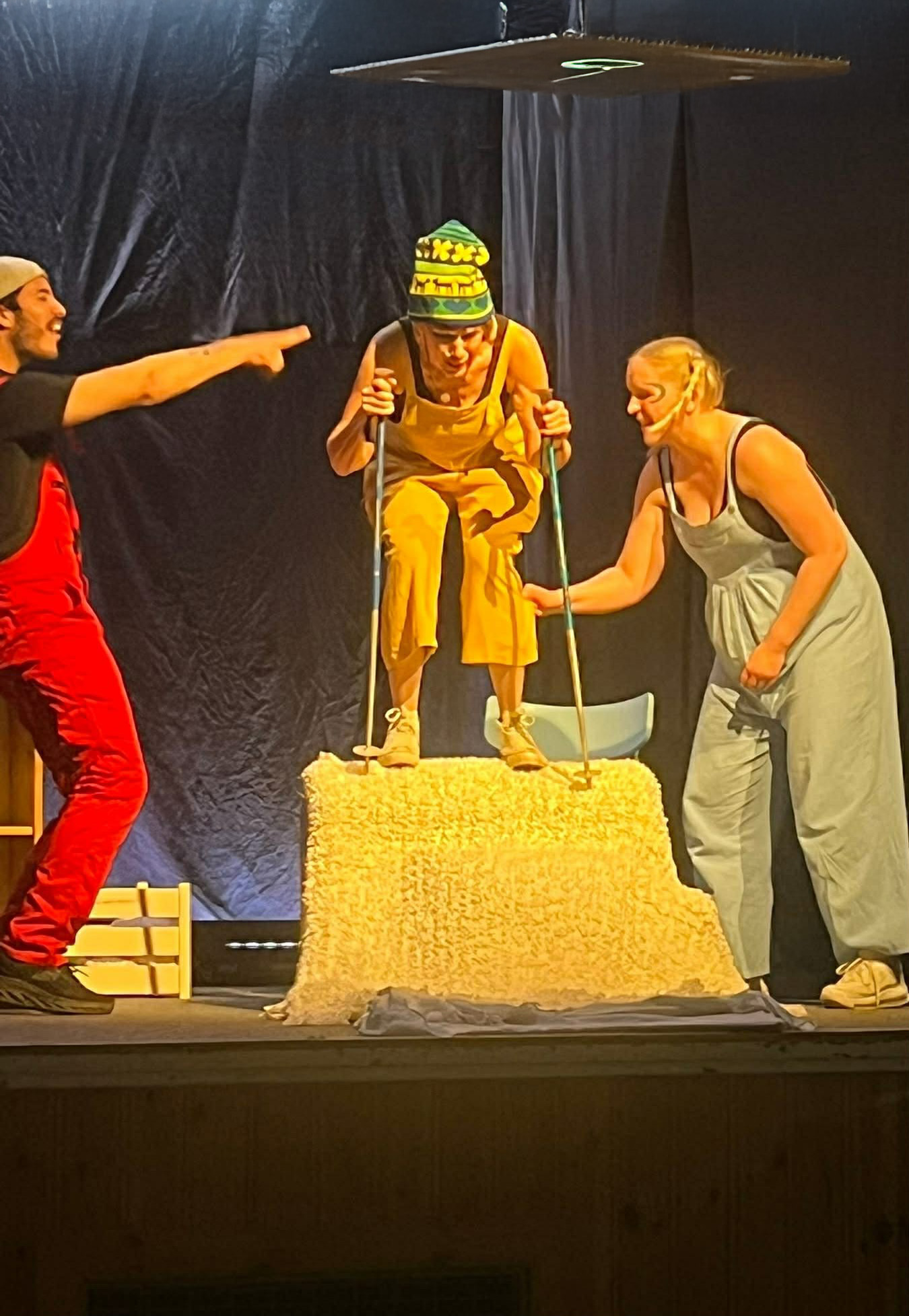 Bildtolkning: En person står på en höjd med skidstavar i händerna. Bredvid står två andra personer som verkar stötta den som är på väg att ge sig utför.