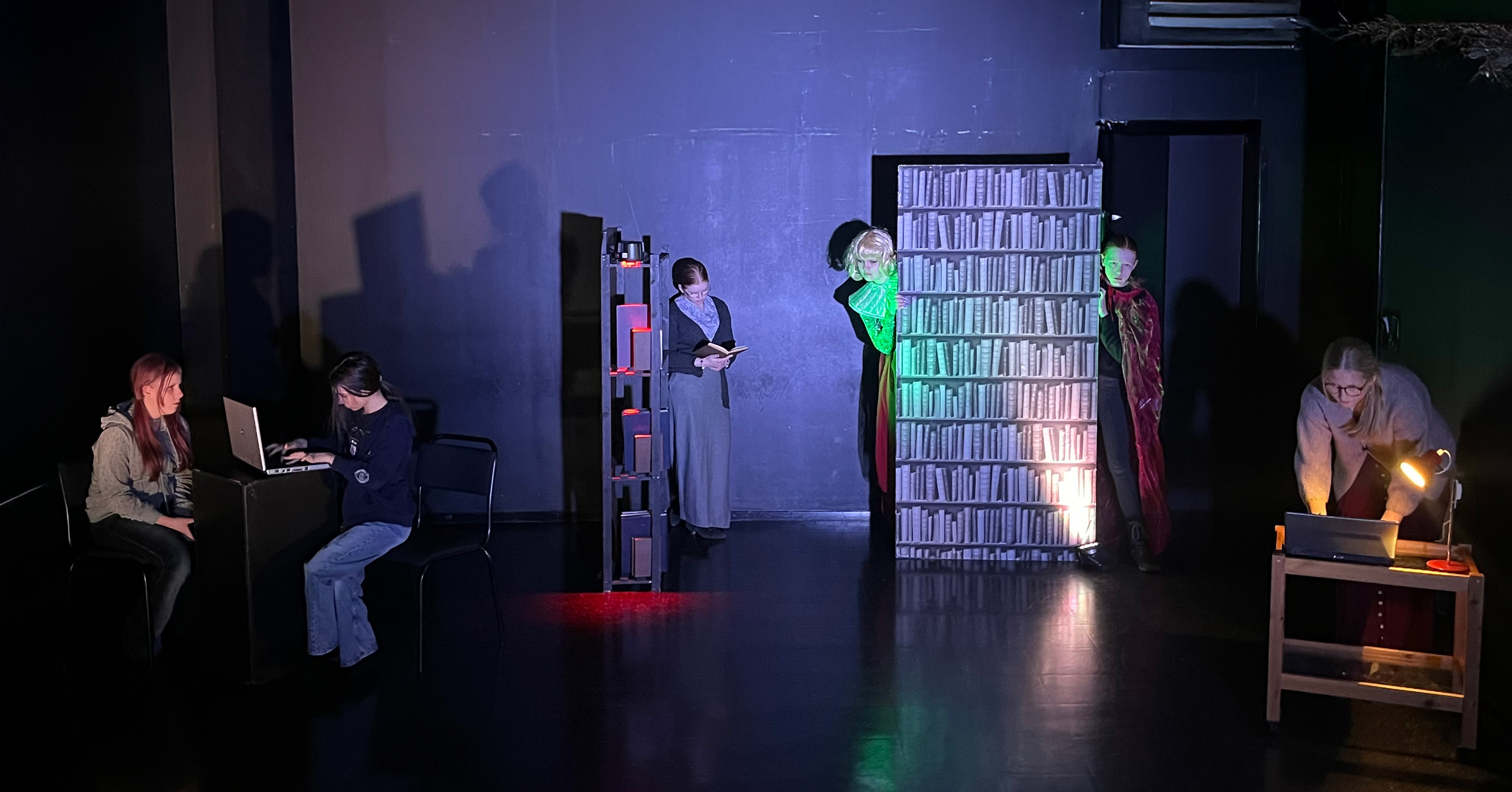 Bildtolkning: Ungdomar befinner sig i ett bibliotek bland hyllor, böcker och kartotek. De verkar leta efter något.