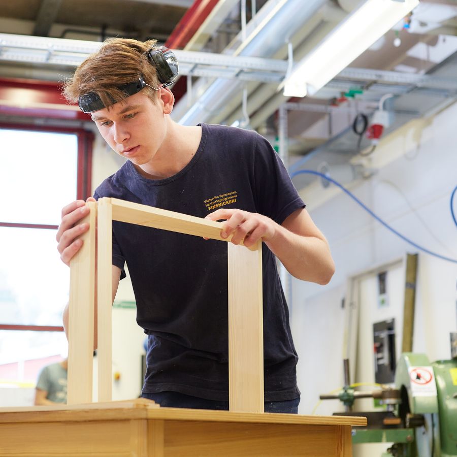 Pojke med hörselskydd i pannan som fokuserar på mått på en träbit. 