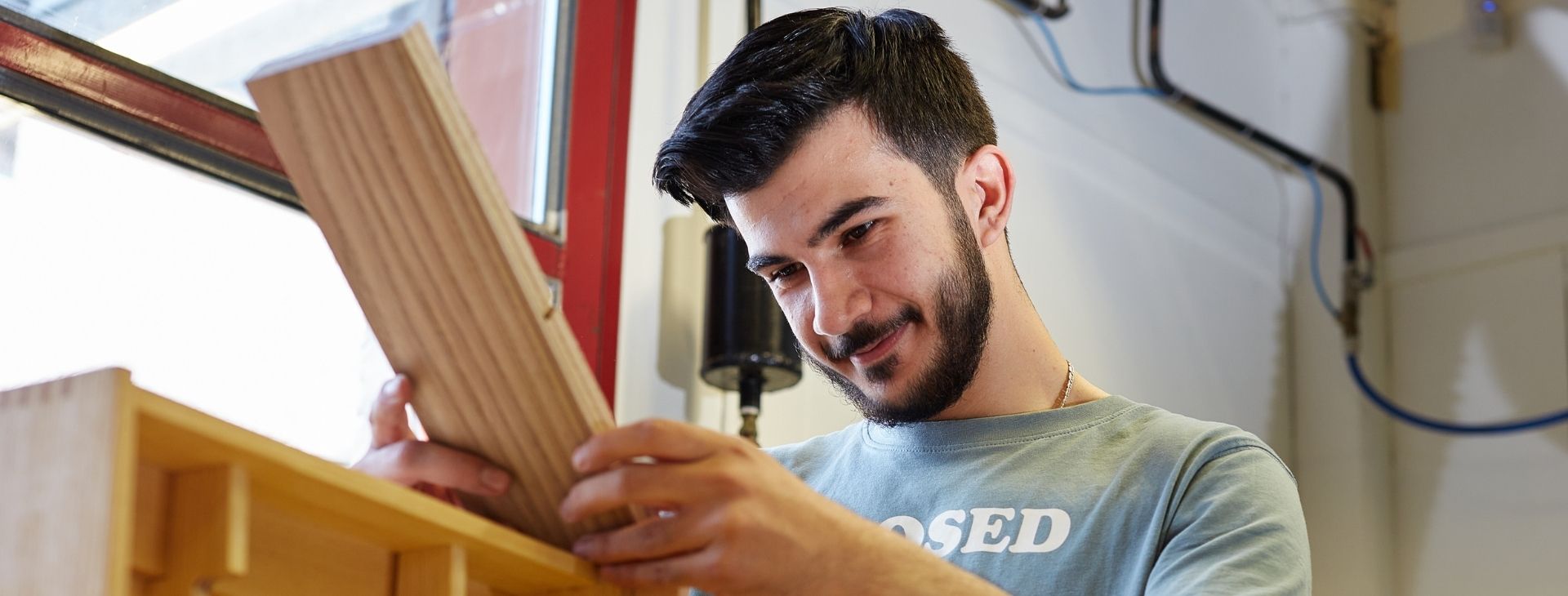 Pojke med mörkt hår som står och arbetar med en träbit.