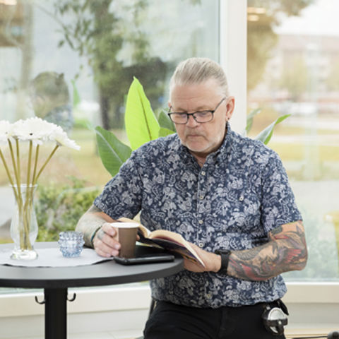 Bild på en man som läser och dricker en kopp te.