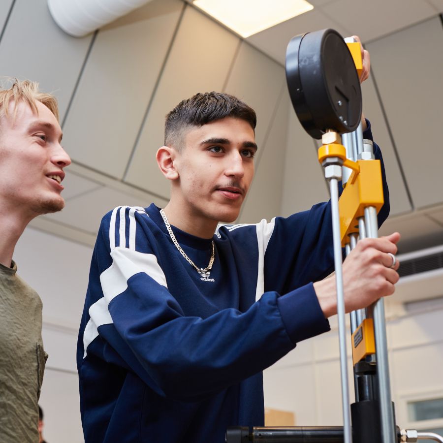 En ljushårig och en mörkhårig pojke som står och tittar och håller på med en maskin.