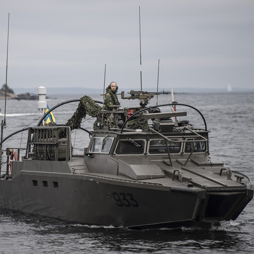 pressbild från Försvarmakten på en av marinens båtar med en soldat som tittar in i kameran och flera soldater i förarhytten