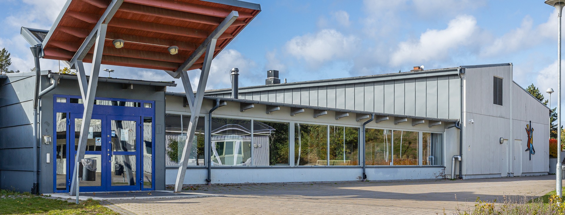 Vit plåtskylt med texten Östra Ringskolan. Skolbyggnader med havet i bakgrunden. 