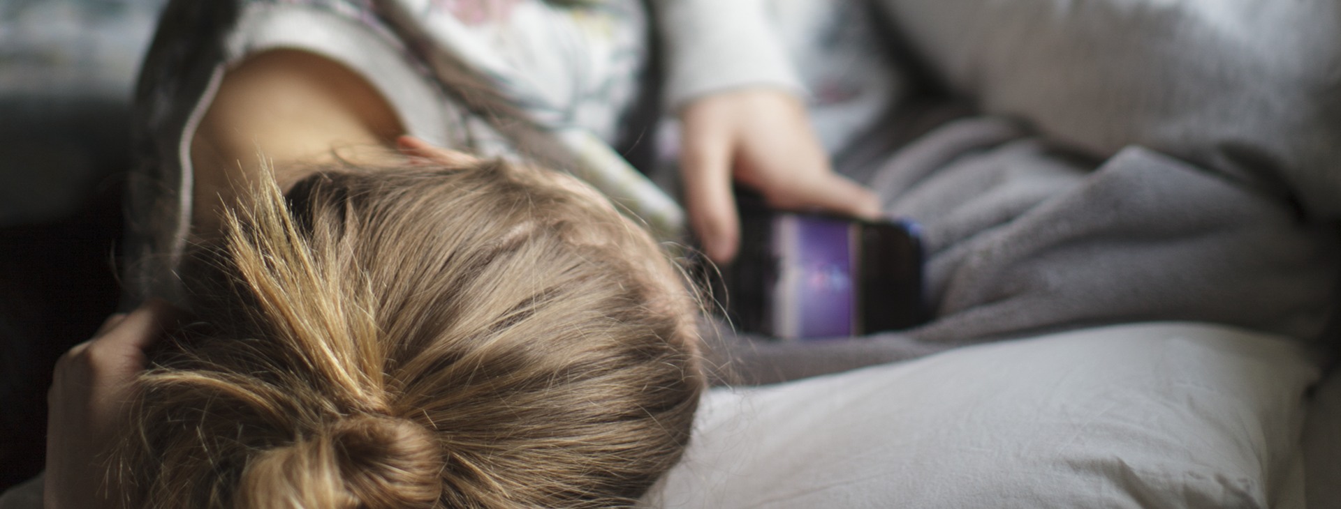 Flicka kollar mobil i säng.