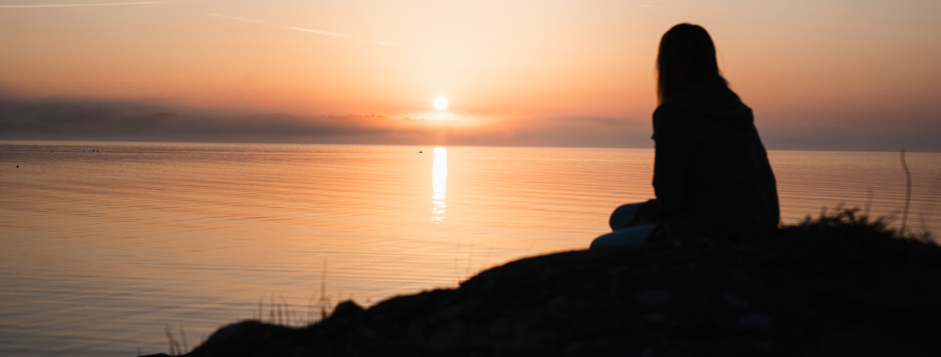Kvinna som sitter vid havet vid solnedgången.